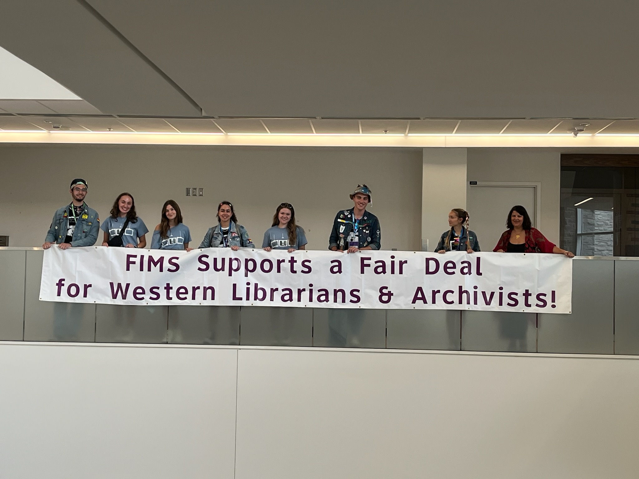 People holding a banner saying "FIMS Supports a Fair Deal for Western Librarians & Archivists"